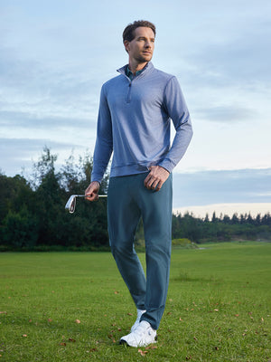 Model in grayish blue stretch plain everyday pants holding a golf club outdoors, full-body shot