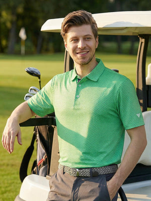 Model in green navy dot performance jersey print polo standing next to a golf cart outdoors, half-body shot