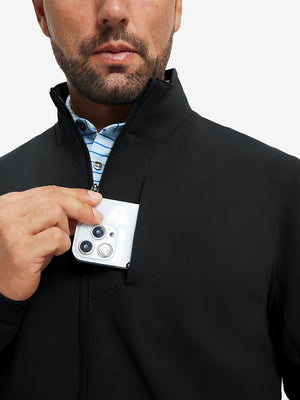 Close detail of hand in chest pocket of water-resistant zip up golf jacket in black.